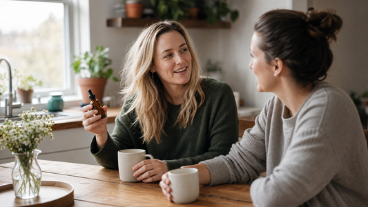 Two people chatting over coffee at a sunny table, one holding a small amber tincture bottle in a relaxed setting