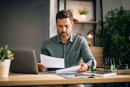 Entrepreneur reviewing CBD wholesale business plan with product samples on desk representing profit margin analysis for CBD resellers